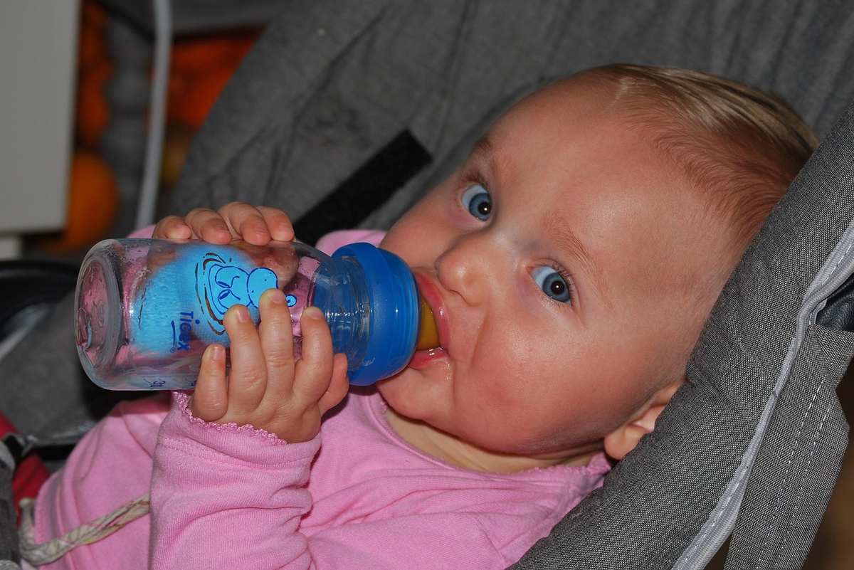 Bébé en rose boit d'un biberon bleu dans un siège gris