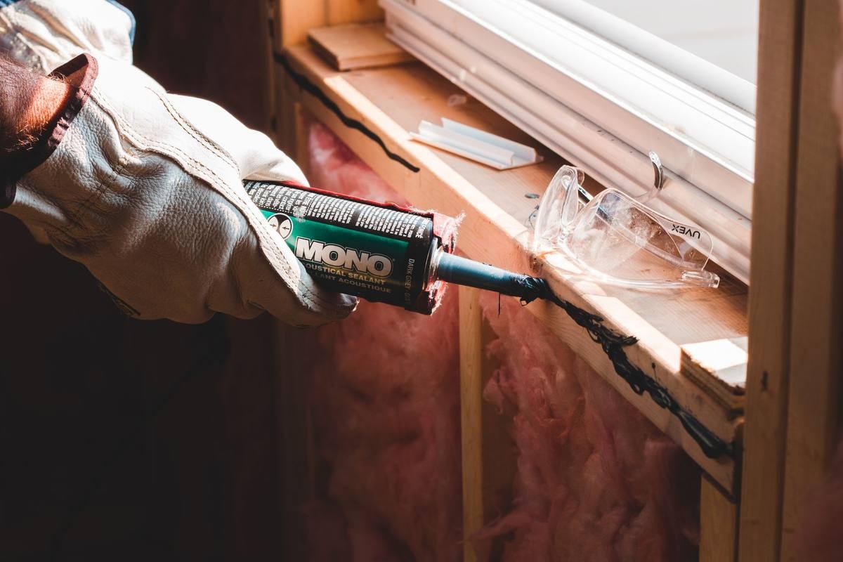 Une main gantée applique du mastic sur le cadre d'une fenêtre